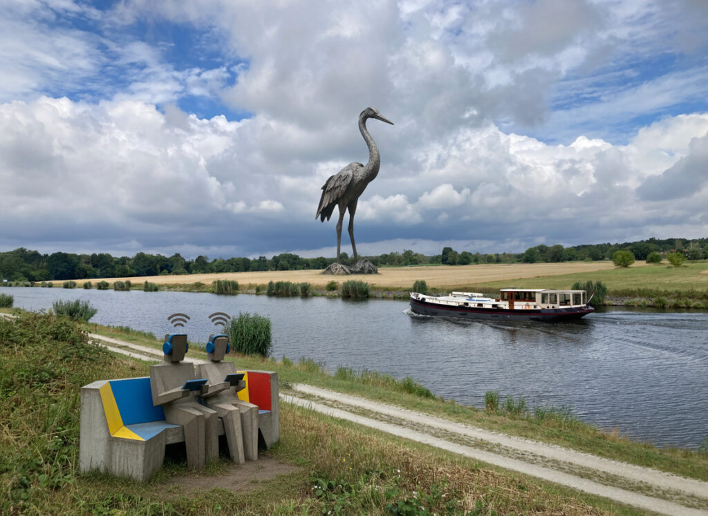 Beispielhafte Darstellung einer überlebensgroßen Kranich-Skulptur und einer kubistischen Sitzbank am Elbe-Havel-Kanal. 