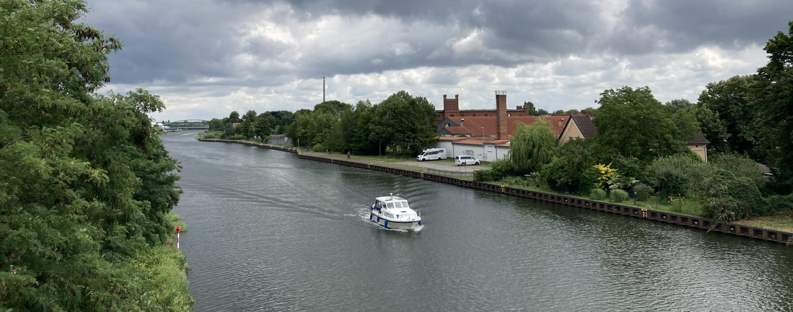 Ein Motorboot fährt auf dem Elbe-Havel-Kanal an einem Backsteingebäude vorbei.